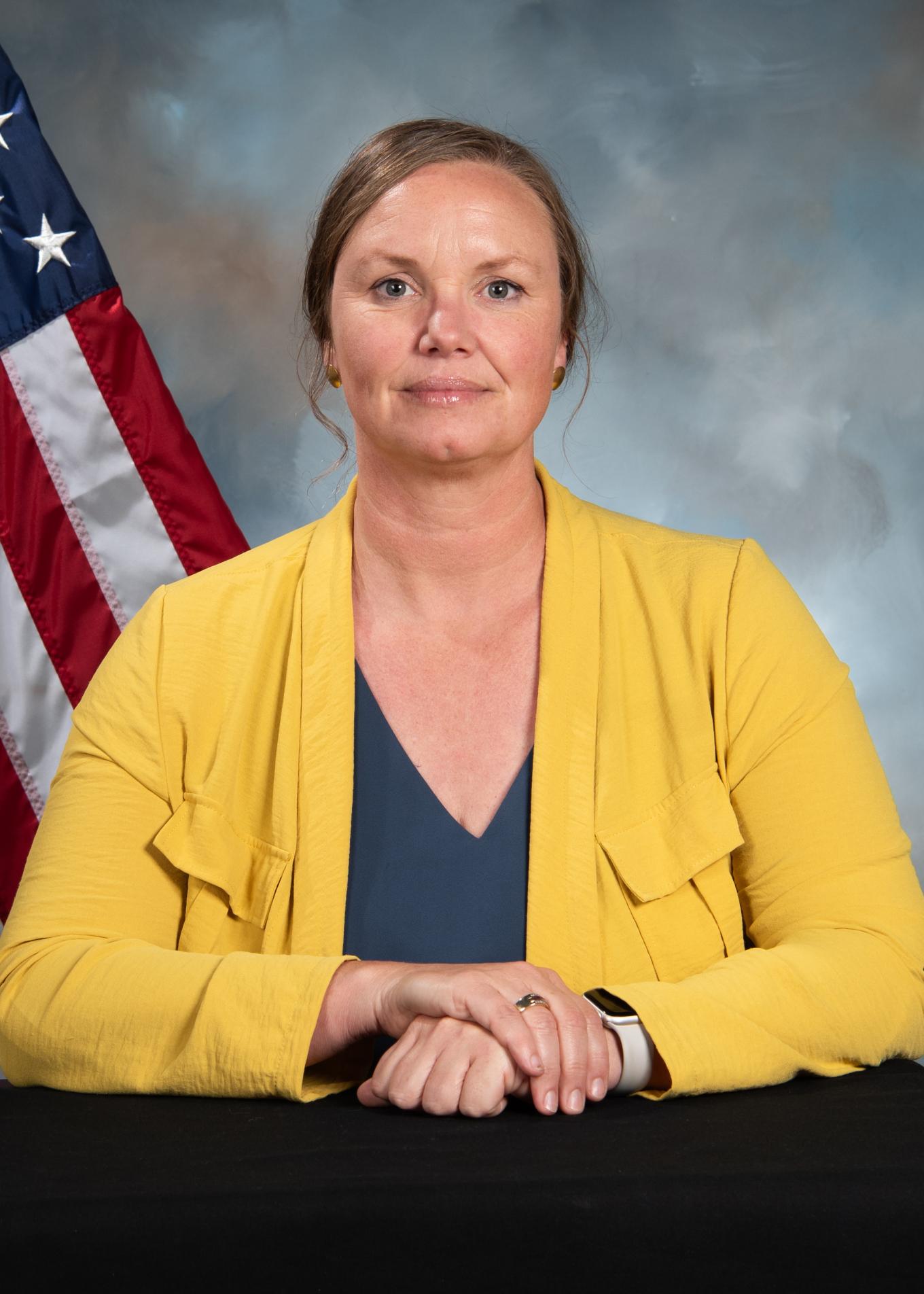 A portrait of a woman in a yellow jacket with a teal shirt